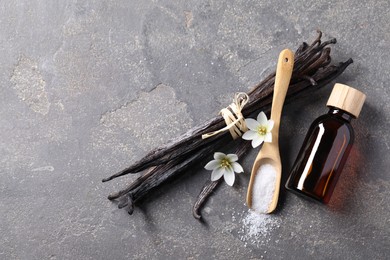 Photo of Spoon with sugar, flowers, vanilla pods and bottle of essential oil on grey textured table, flat lay. Space for text