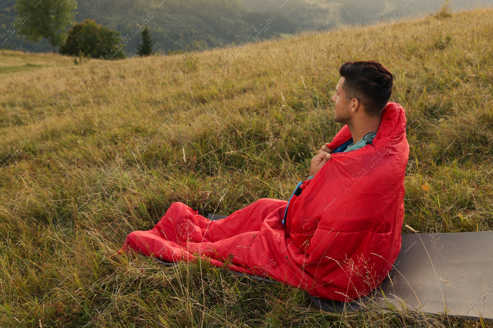 Photo of Man in sleeping bag on hill, space for text