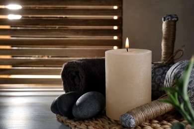 Photo of Burning candle, herbal bags and spa stones on wooden table, space for text