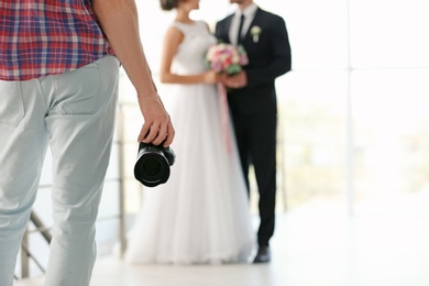 Photo of Professional photographer with camera and wedding couple in studio