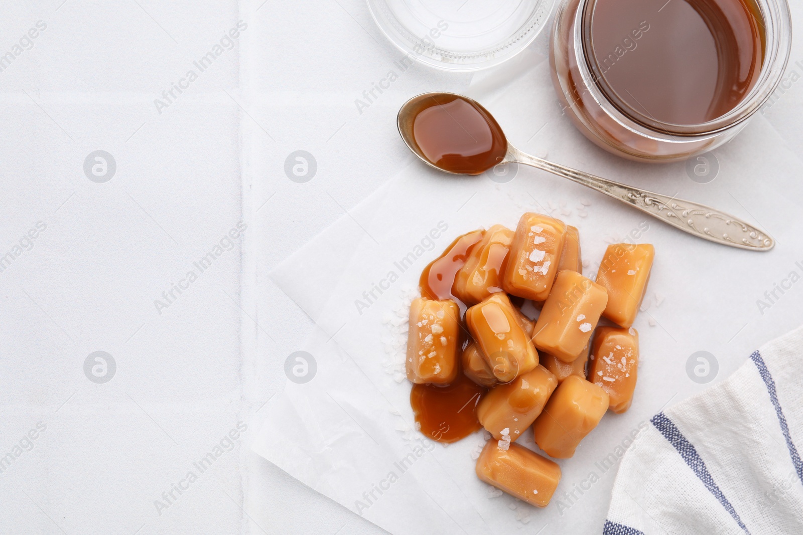 Photo of Yummy caramel candies and sea salt on white table, flat lay. Space for text