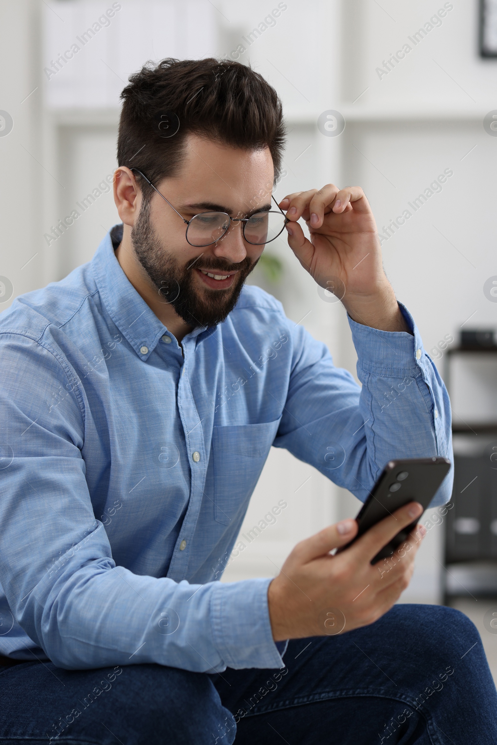 Photo of Handsome young man using smartphone in office