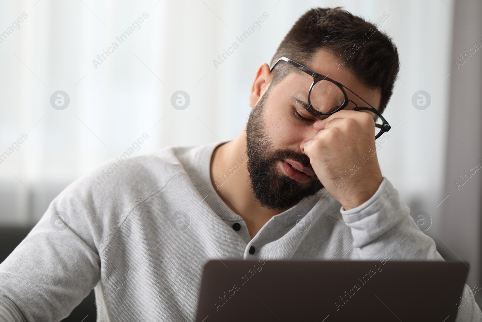 Photo of Man with glasses suffering from headache at workplace in office