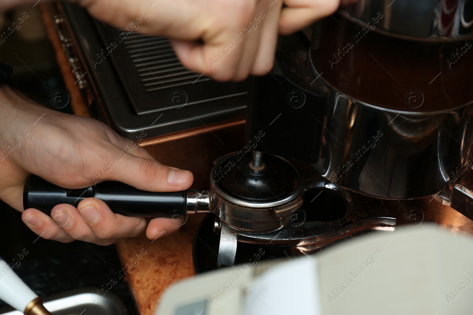 Photo of Barista pressing ground coffee with tamper in portafilter, closeup