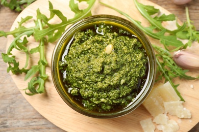 Photo of Bowl of tasty arugula pesto and ingredients on wooden board, flat lay