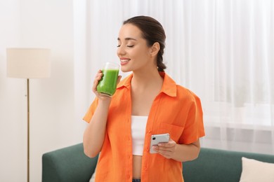 Photo of Beautiful young woman drinking delicious smoothie at home