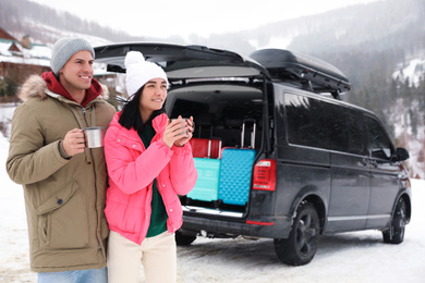 Photo of Happy couple with drinks near car on snowy road. Winter vacation