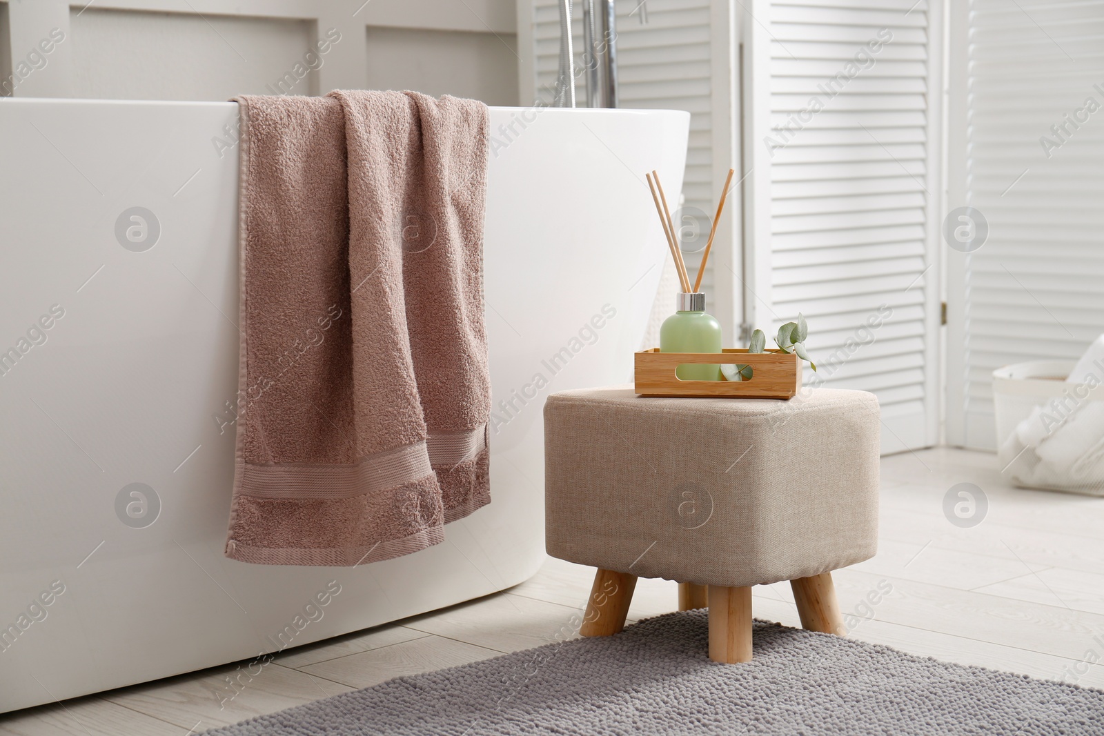 Photo of Stylish ottoman with air reed freshener on floor in modern bathroom. Interior design