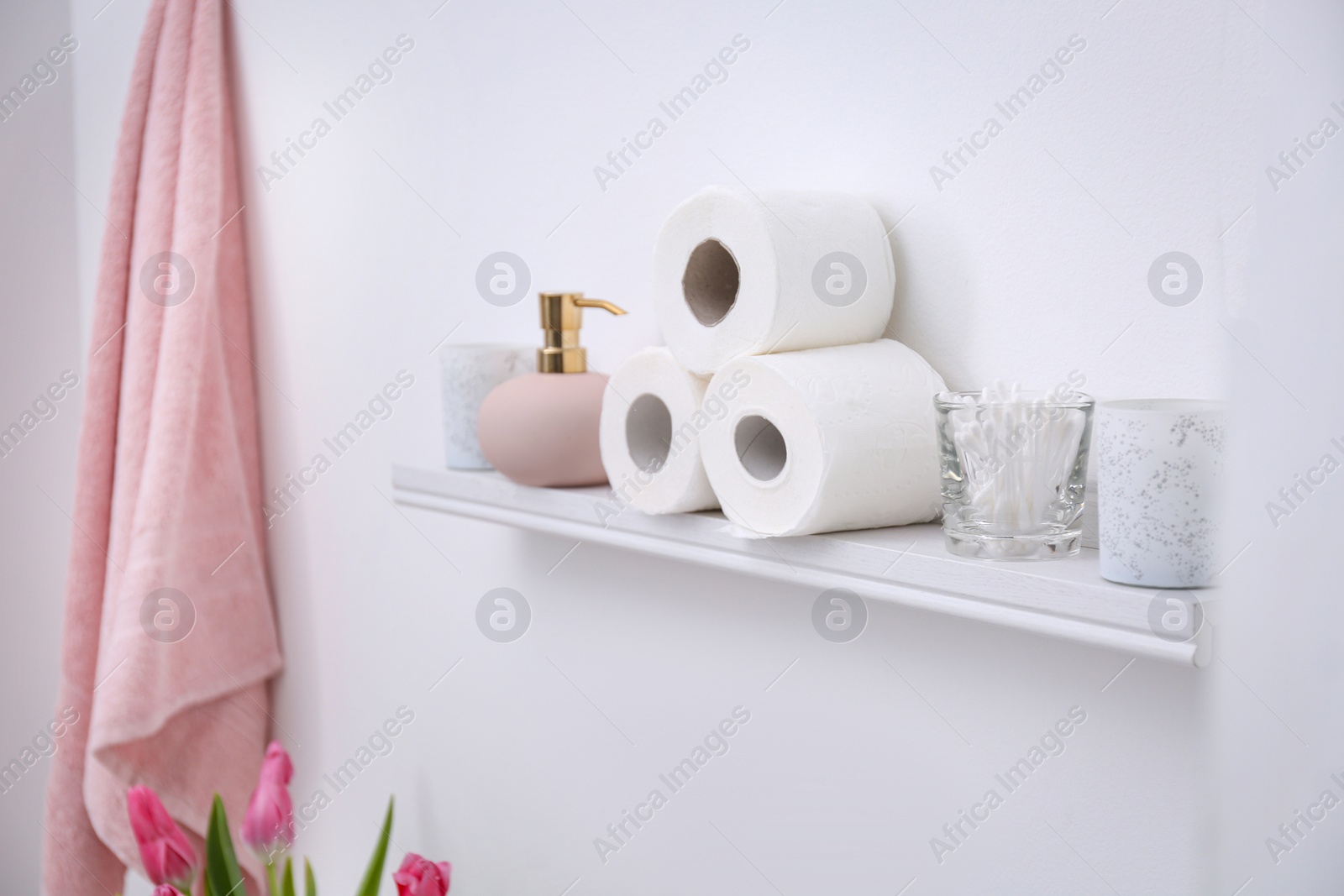 Photo of Toilet paper rolls, soap dispenser and cotton swabs on shelf in bathroom