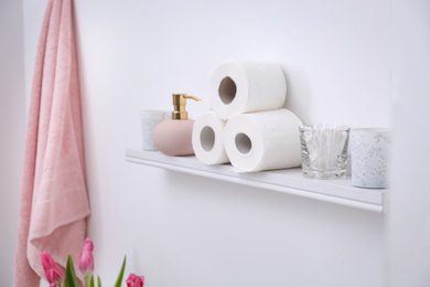 Toilet paper rolls, soap dispenser and cotton swabs on shelf in bathroom