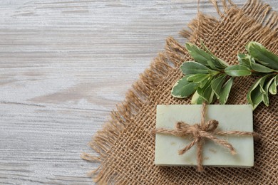 Soap bar and green plant on wooden table, top view with space for text