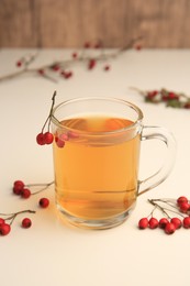 Photo of Cup with hawthorn tea and berries on beige table, closeup