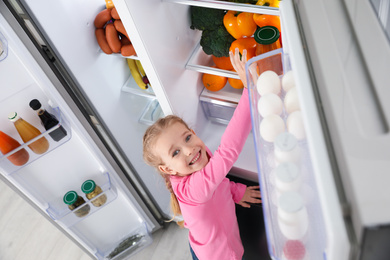 Photo of Little girl taking bell pepper out if refrigerator indoors, above view