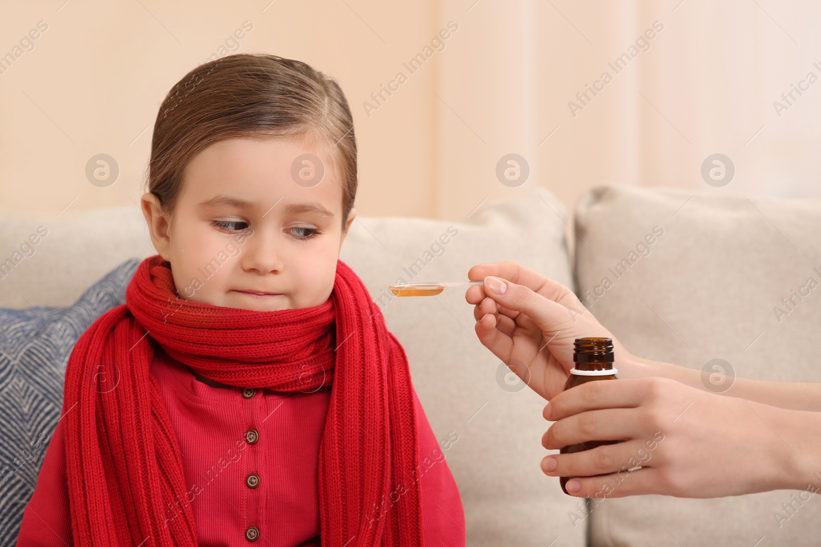 Photo of Mother giving cough syrup to her daughter on sofa indoors