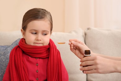 Mother giving cough syrup to her daughter on sofa indoors