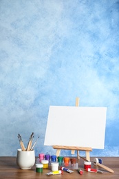 Wooden easel with blank canvas board and painting tools for children on table near color wall