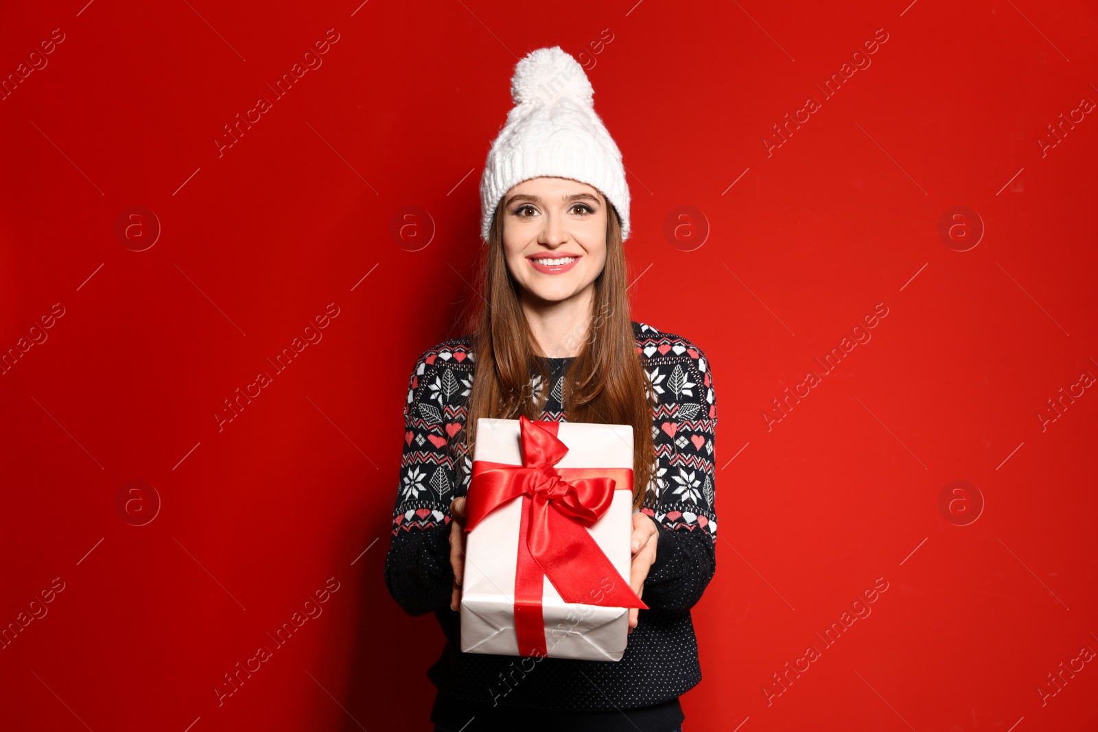 Photo of Young woman in Christmas sweater holding gift box on red background