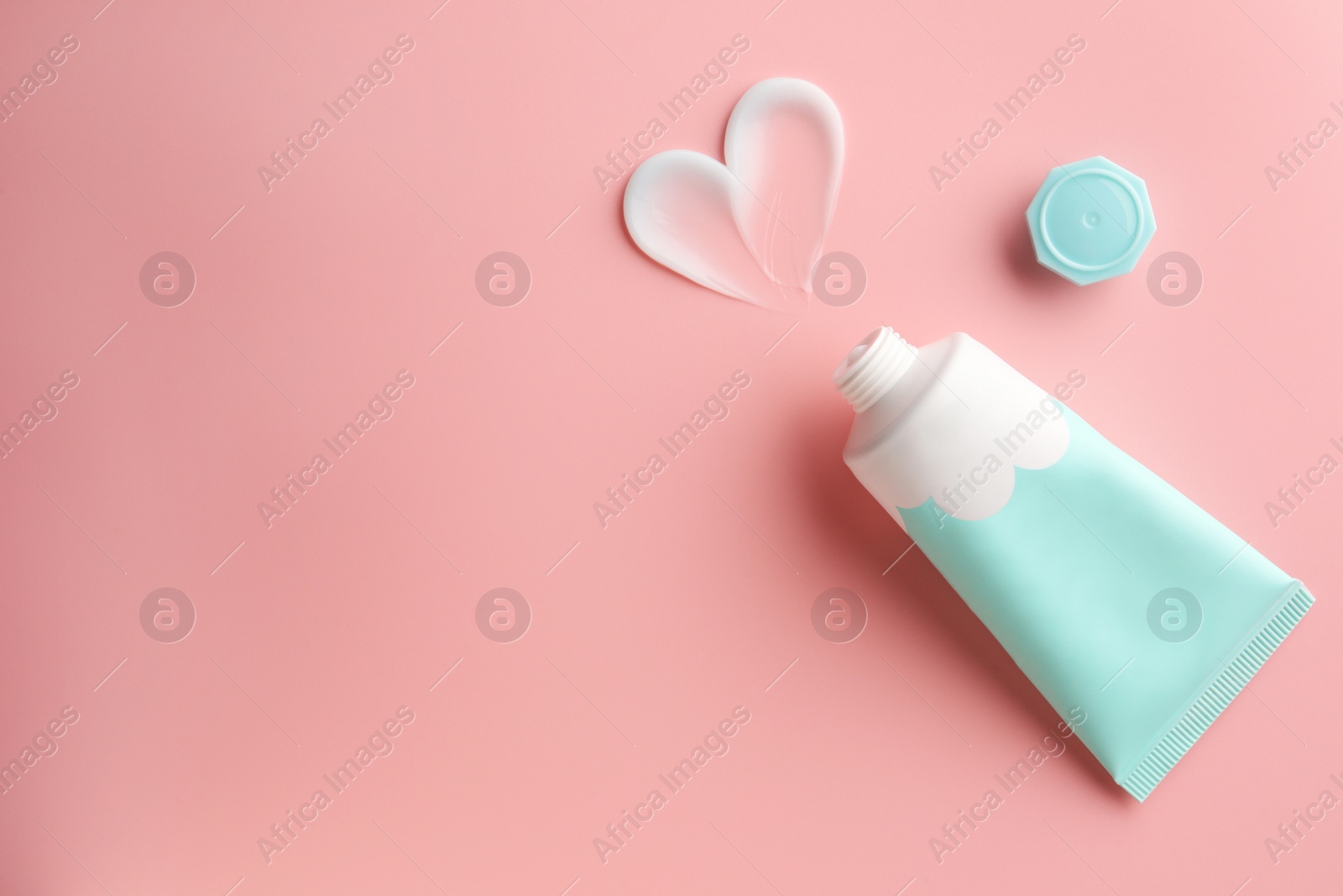 Photo of Tube and sample of facial cream on pink background, top view. Space for text