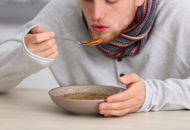 Photo of Sick young man eating soup to cure flu at table