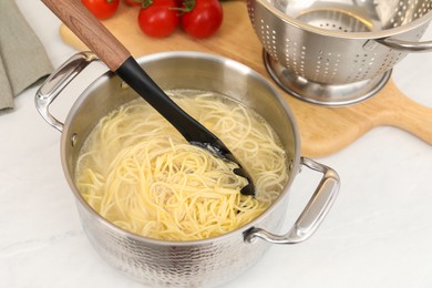 Cooked spaghetti and pasta server in metal pot on white countertop, closeup