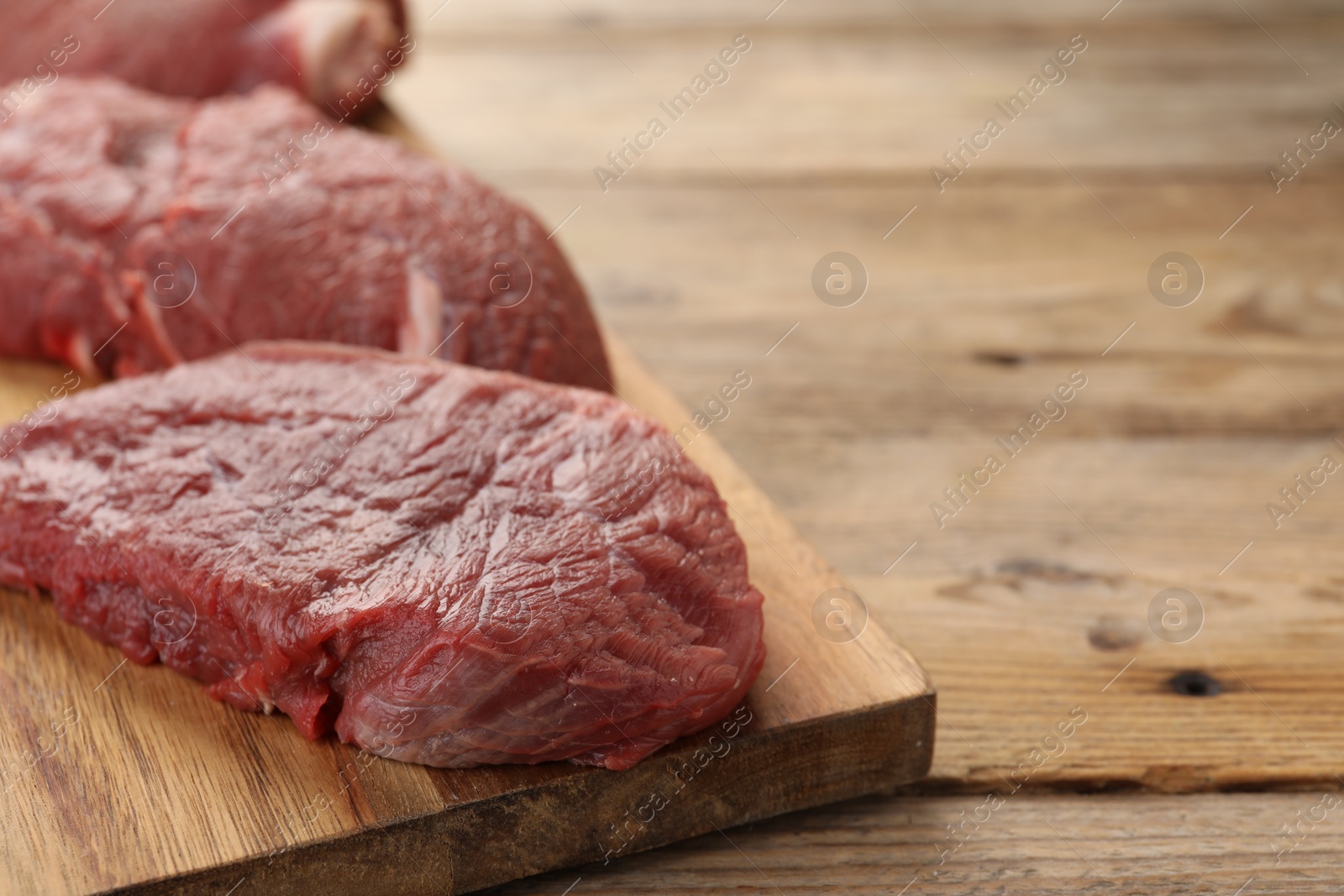 Photo of Pieces of raw beef meat on wooden table, space for text