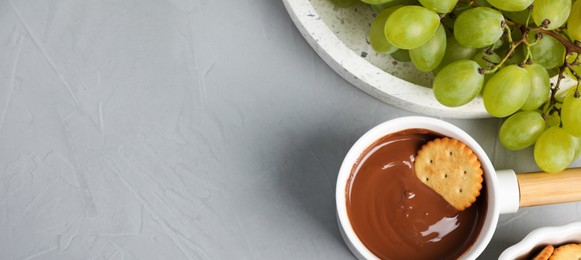 Dipping cookie into pot with chocolate fondue on grey table, flat lay with space for text. Banner design