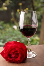 Photo of Glass of red wine and rose flower on wooden table outdoors