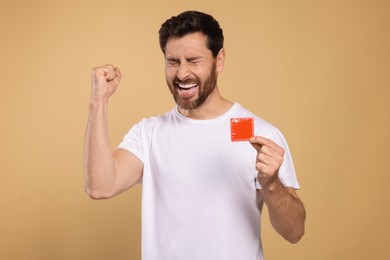 Emotional man holding condom on beige background. Safe sex