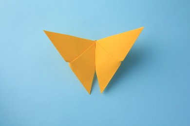 Photo of Origami art. Handmade yellow paper butterfly on light blue background, top view