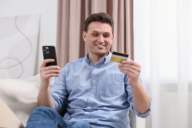 Photo of Happy man with credit card and smartphone shopping online at home