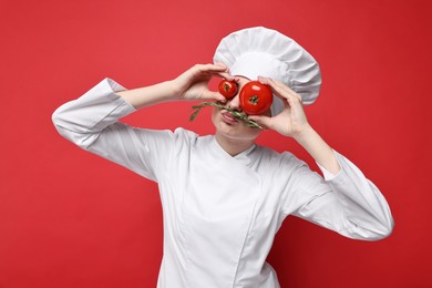 Photo of Professional chef with fresh rosemary and tomatoes having fun on red background