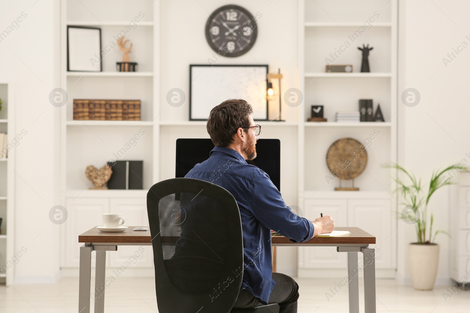 Photo of Home workplace. Man working at wooden desk in room, back view