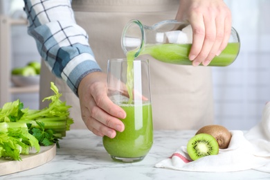 Photo of Woman pouring fresh celery juice into glass at white marble table, closeup