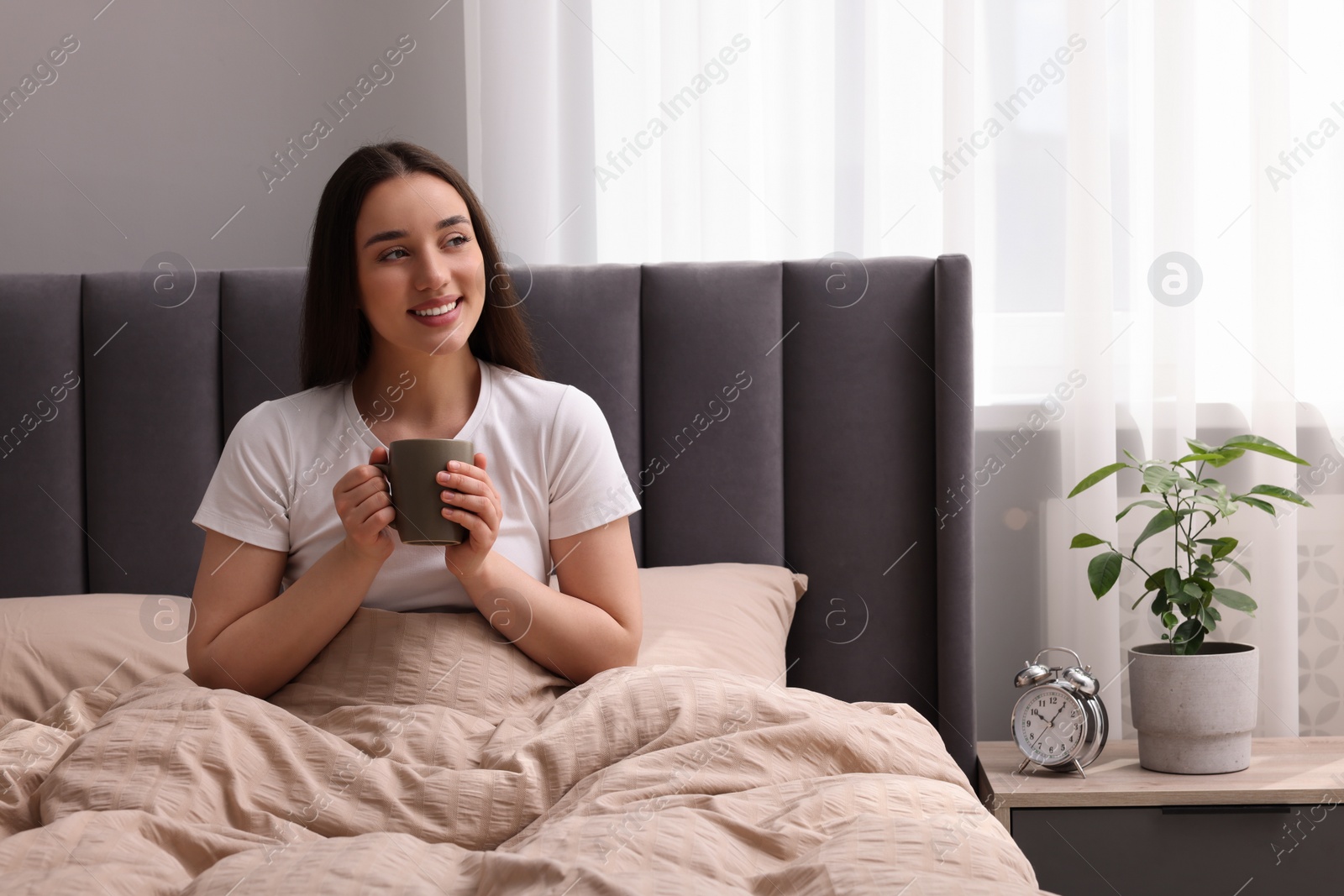 Photo of Beautiful woman with cup of drink on bed at home. Lazy morning