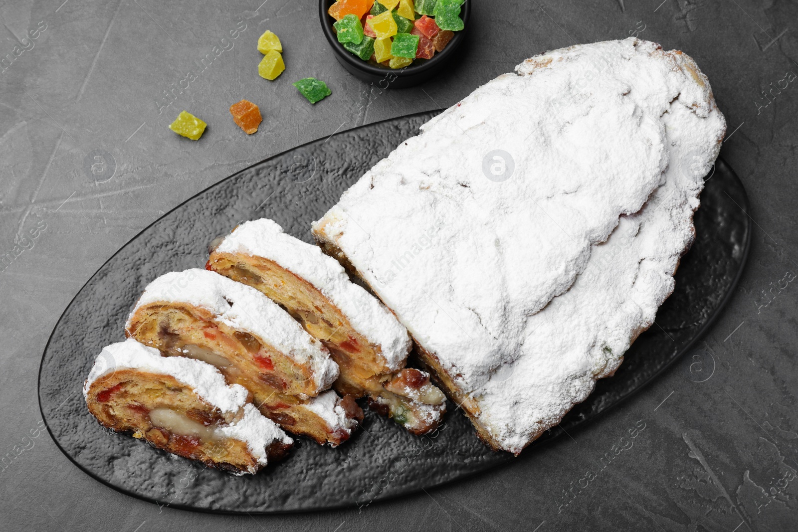 Photo of Traditional Christmas Stollen with icing sugar on black table, flat lay