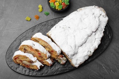 Photo of Traditional Christmas Stollen with icing sugar on black table, flat lay