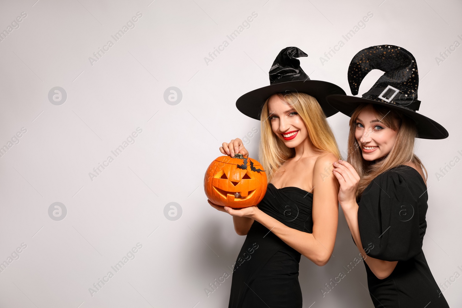 Photo of Beautiful women in witch costumes with jack o'lantern on white background, space for text. Halloween party