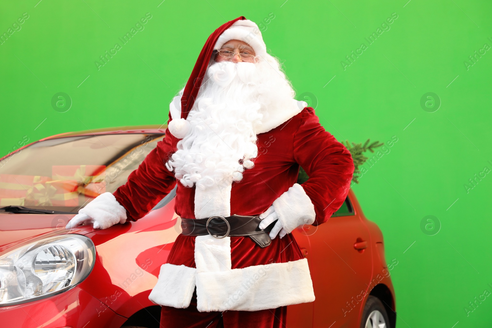 Photo of Authentic Santa Claus near car with fir tree and presents against green background