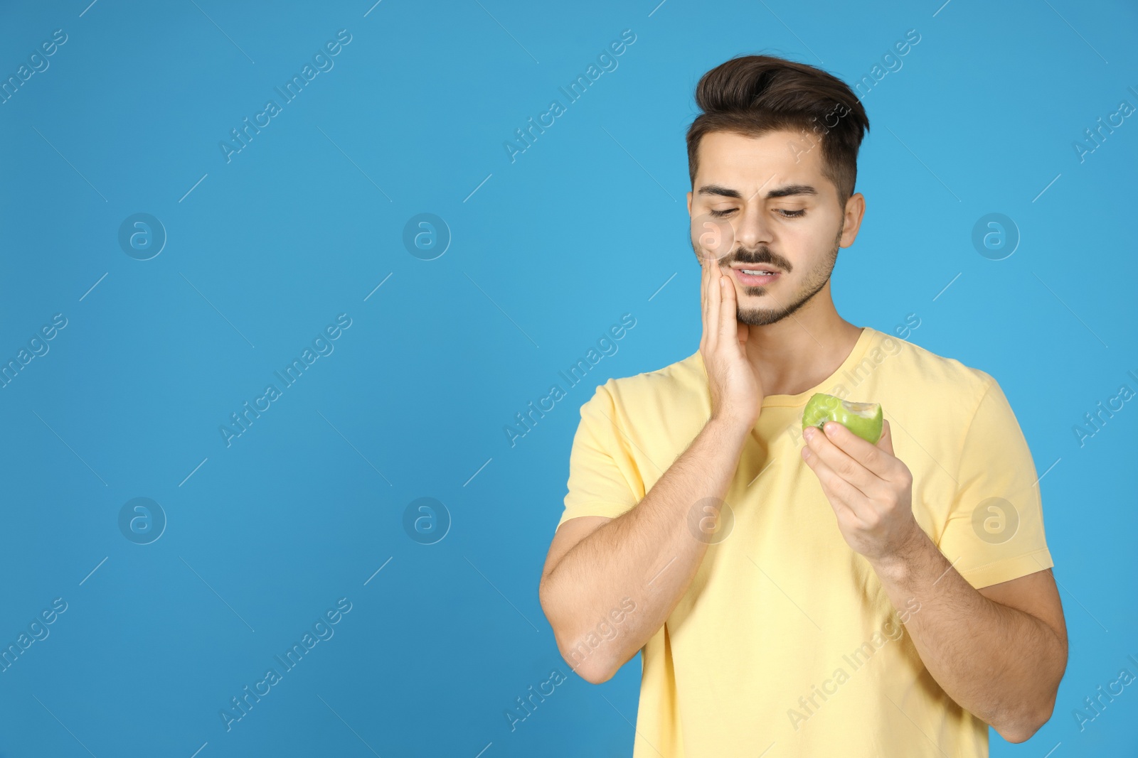 Photo of Emotional young man with sensitive teeth and apple on color background. Space for text