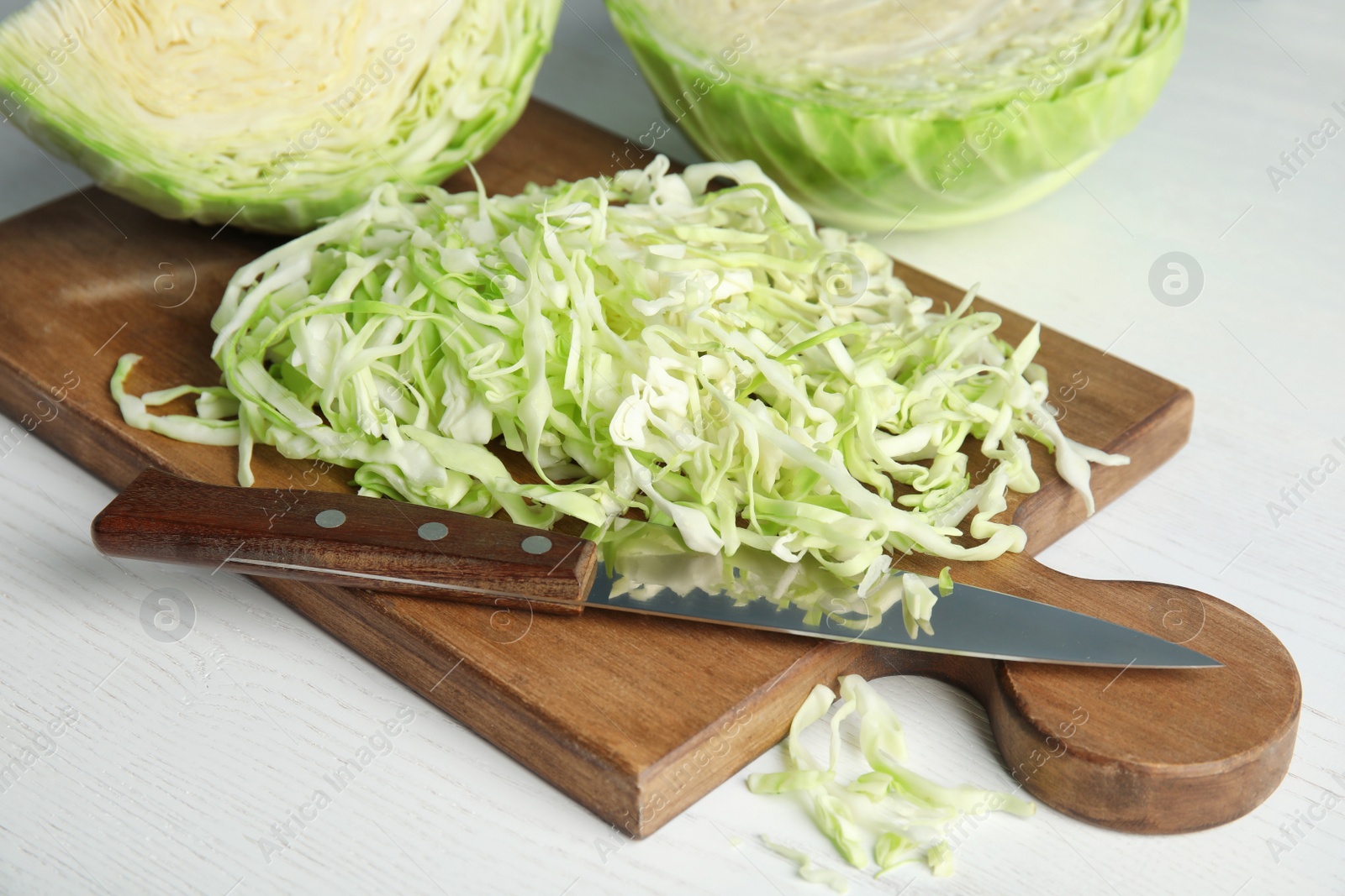 Photo of Cutting board with chopped and sliced cabbage on table