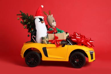 Photo of Child's electric car with toys, gift boxes and Christmas tree on red background