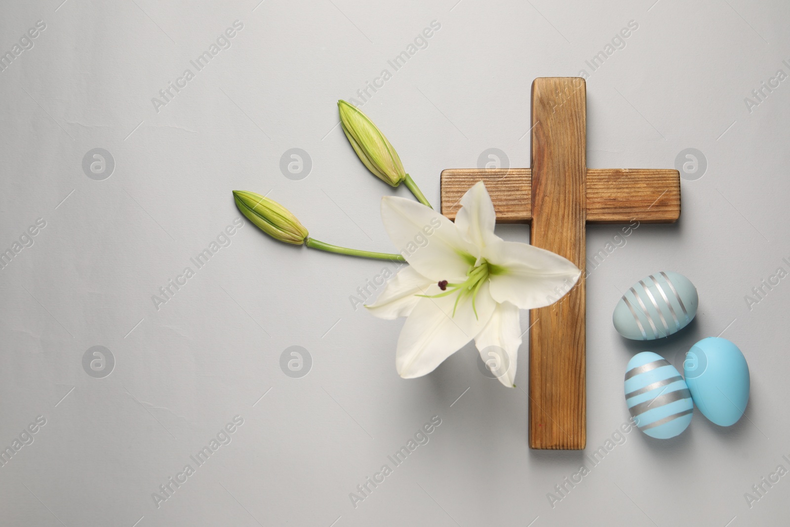 Photo of Wooden cross, painted Easter eggs and lily flowers on grey background, flat lay. Space for text