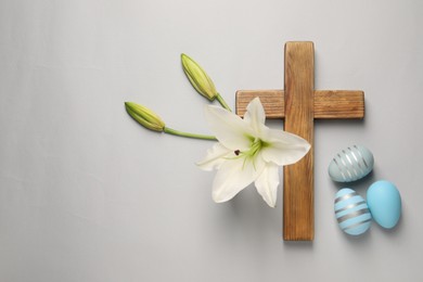 Photo of Wooden cross, painted Easter eggs and lily flowers on grey background, flat lay. Space for text