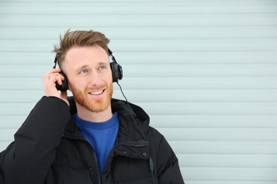 Photo of Young man listening to music with headphones against light wall. Space for text