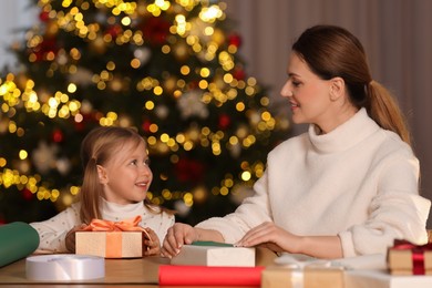 Christmas presents wrapping. Mother and her little daughter decorating gift boxes at home