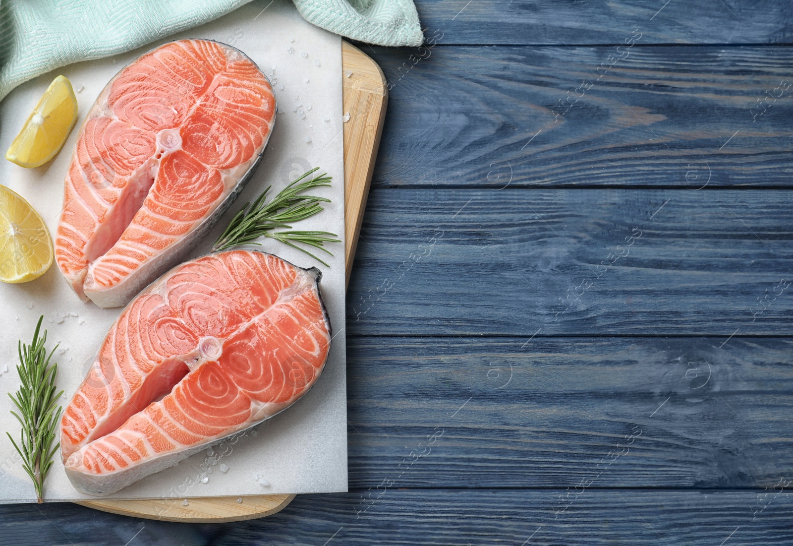 Photo of Top view of fresh raw salmon with lemon and rosemary on blue wooden table, space for text. Fish delicacy