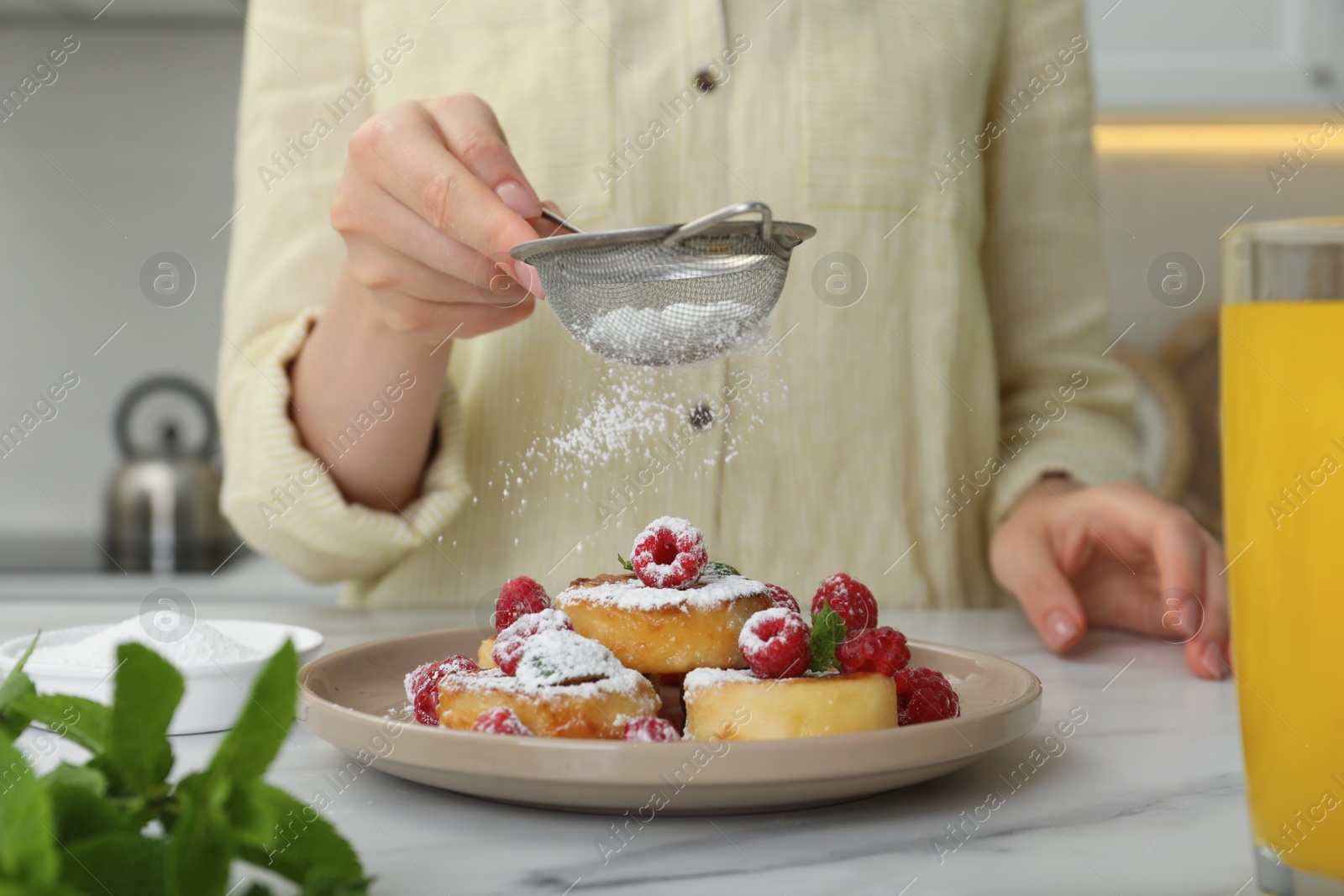 Photo of Woman sieving powdered sugar on cottage cheese pancakes at white table, closeup