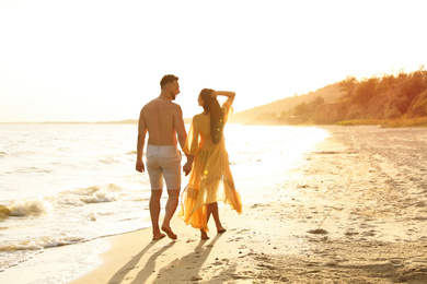 Happy couple walking together on beach at sunset, back view