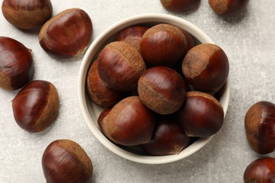 Bowl with roasted edible sweet chestnuts on light grey table, flat lay
