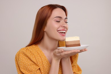 Photo of Young woman with piece of tasty cake on light grey background